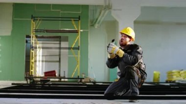 İnşaat alanındaki kablosuz kulaklıklardan müzik dinlerken kameranın önünde dans eden iyi görünümlü inşaat işçisi inşaat malzemeleri boyuyor. ARRI Alexa Mini 'de çekilen.