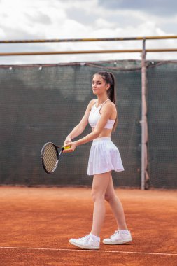 Yaz günü karizmatik profesyonel tenisçi kadın tenis topunu dışarıda tenis kortunda çaldığı raketle ısıtıyor..