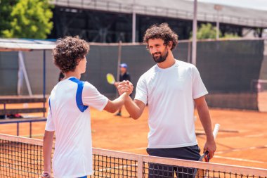 Two paddle tennis players high-fiving their hands at the end of the match on the green court at sunset.
