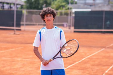 Tenis kortunda raketi olan genç bir tenisçi..