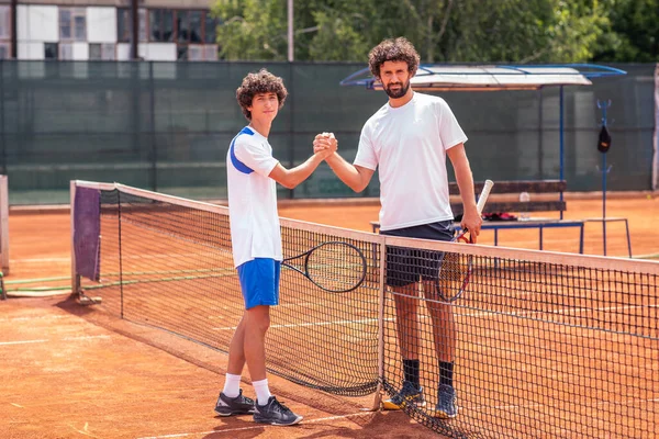 senior and young man shake hands before tennis match.