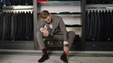 Good looking Caucasian man in a casual suit take a pair of leather shoes and wear them on the luxury suit shop. Shot on ARRI Alexa Mini