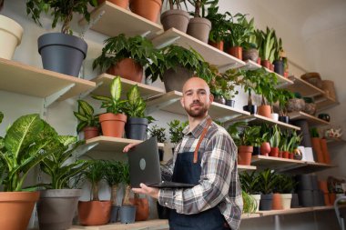 Çiçekçide çiçekçinin sahibi çiçekçide çiçekçiye gider ve dizüstü bilgisayarla mağazanın envanterini kontrol eder. Dükkanın sahibi odur. Portre