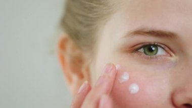 Yeşil gözlü genç bir kadının videosunu çekerken çekinde nemlendirici krem var. Cilt bakımı konseptindeki ürünlere masaj yapmak için parmağını kullanıyor. 4k