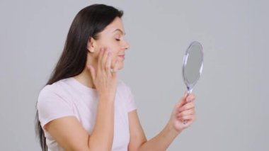 Adult woman on white background holding a mirror on hand and looking at their face very carefully in front of the camera. Shot on ARRI Alexa Mini