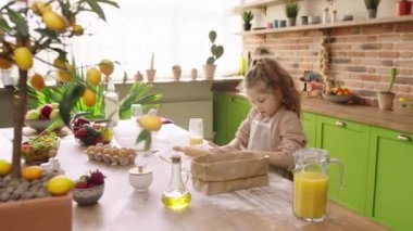 Beautiful green kitchen amazing cute little girl with curly hair preparing the dough for delicious dessert she using the kitchen roller and some flour. Shot on ARRI Alexa Mini