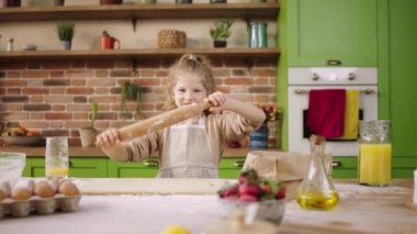 Charismatic and happy little girl while preparing the delicious dessert for all family take the kitchen roller and dancing at kitchen table in a modern kitchen at home. Shot on ARRI Alexa Mini