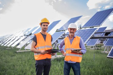 Walking in front of the camera the two charismatic men workers examining solar batteries and communicating of business they walking between rows.