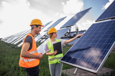 Two technician lady and man analysing together and discussing about cleanliness of photovoltaic solar panels they standing in the middle of solar power farm.
