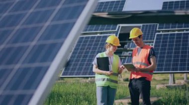 Two technician lady and man analysing together and discussing about cleanliness of photovoltaic solar panels they standing in the middle of solar power farm. 4k