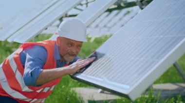 Closeup to the camera in a sunny day investor man mature looking touching his photovoltaic solar panels and analysing the cleanliness of the batteries.