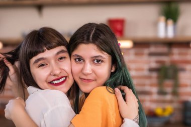 Lesbian couple very beautiful two females embracing with LGBT rainbow flag in the kitchen looking to the camera and smiling large. Portrait