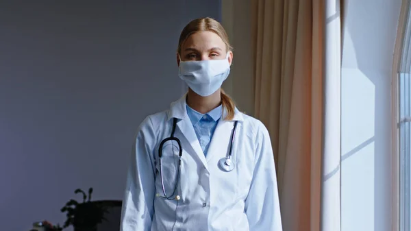 Pretty young lady doctor take her protective mask and wearing on face and looking sad to the panoramic window.