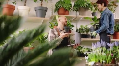In front of the camera shop assistant man together with the florist woman working together they checking the inventory from the shop using the laptop and discussing at the same time. 4k