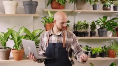 Caucasian entrepreneur man in the floral store using the laptop to checking the inventory of shop then looking to the camera smiling large. Shot on ARRI Alexa Mini
