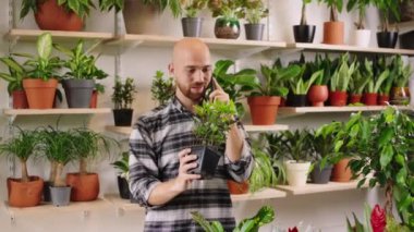 In the floral store the customer guy Caucasian looking take some flowers from the shop shelves and have a conversation with someone on the smartphone. 4k