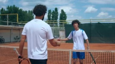 Two charismatic tennis players father and son before match shaking hands over the tennis net outdoor on the clay tennis court. 4k