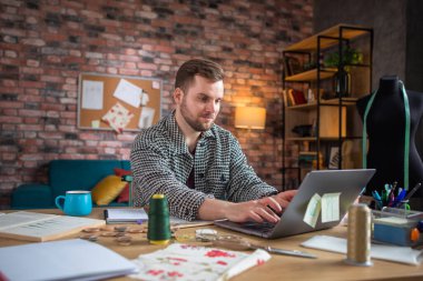 Çalı sakallı yakışıklı bir adam mankeni ölçerken elbise tasarlıyor..