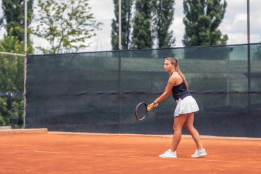 On the outdoor tennis court professional young female tennis player hitting hard the tennis ball with the racket.