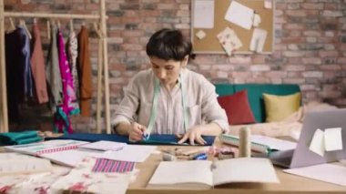 At fashion atelier and tailoring in front of the camera amazing looking fashion designer woman sew some clothes then looking up to the camera and smiling large. Shot on ARRI Alexa Mini