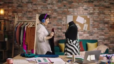 Large modern tailoring atelier beautiful dressmaker make some measurements of mannequin and hugging excited her mannequin while listening music from the headphones. Shot on ARRI Alexa Mini