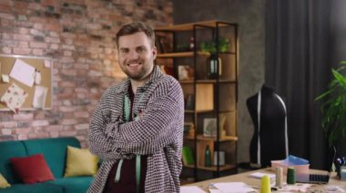 Smiling large charismatic fashion designer posing in front of the camera he crossing hands standing beside his working place ate the tailoring atelier. 4k