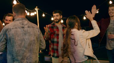 Group of young people have a party on the rooftop of terrace they are drinking some champagne and enjoy the evening smiling large and hugging each other. Dance