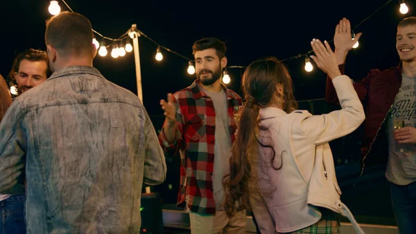 Group of young people have a party on the rooftop of terrace they are drinking some champagne and enjoy the evening smiling large and hugging each other. Dance