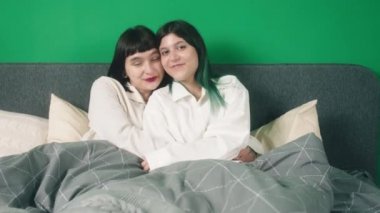 Amazing ladies young looking lesbian couple posing in front of the camera while laying on the bed together hugging each other with love and looking straight. 4k