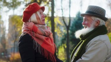 Amazing beautiful old woman and old man charismatic and casual have a good time together in the middle of the park have a conversation in front of the camera they hugging each other in a cold autumn