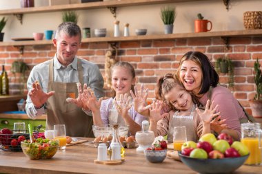 At the large kitchen island happy excited parents together with their two daughters preparing the dough for a delicious dessert dad hard mixing the dough mommy and daughters are helping him. Portrait