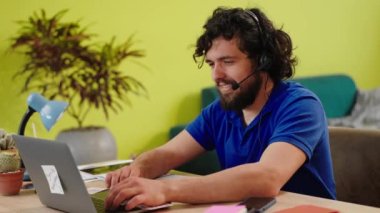 Handsome guy working online at call centre from home using the the laptop he type something and he wear the headset to discussing with client. 4k