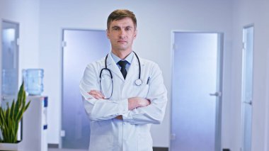 Portrait of a man doctors with a serious face in front of the camera looking straight have a stethoscope on the neck he stand in the hospital corridor. Portrait