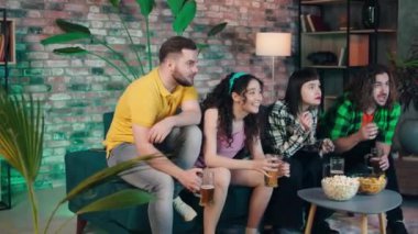 At home in living room group of multiracial friends very charismatic and enthusiastic watch a football match on tv channel they take some snacks and beer. Shot on ARRI Alexa Mini