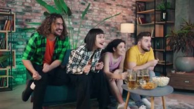 Group of multiracial friends together watching on tv on sport channel a football match they getting excited when favourite team wins they screaming and jumping over the sofa. Shot on ARRI Alexa Mini
