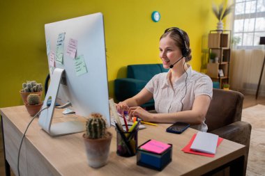 Mature businesswoman in headset speaking by conference call while looking at computer. Home office. Portrait