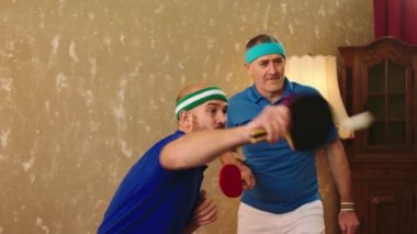 Taking video closeup to the camera two excited with a large smile men one old and young plying the table tennis they hugging each other and feeling great. 4k