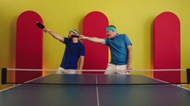 Father and son very handsome together dancing before to start the ping pong game they holding the rackets on hands smiling large and enjoy the moment together. 4k