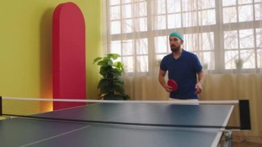 Good looking guy playing on the ping pong game he catch the balls and hitting with the red paddles the guy are wearing in the table tennis uniform. Shot on ARRI Alexa Mini