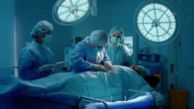 A lower shot of a surgeon giving an operation to someone while wearing surgical gear and having two assistant nurses by his side. Shot on ARRI