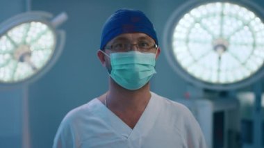 A male doctor standing in a surgery room wearing glasses a hairnet and a medical mask staring into the camera as it s closing in. Shot on ARRI