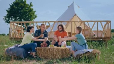 In the middle of campsite group of young and good looking friends enjoy the time together while sitting on the haystack and chatting all together. Shot on ARRI