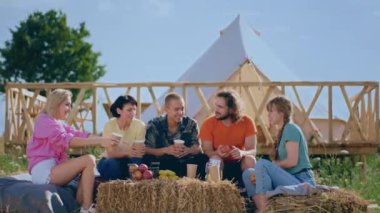 Very happy and excited group of friends at campsite enjoy the time together while sitting on the haystack they discussing together and have fun.
