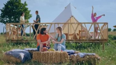 At campsite in the morning couple enjoy the breakfast while drinking juice they discussing and feeling relaxed other people wake up and get relaxed and enjoy the fresh air beside the tent. 4k