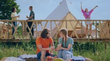 Romantic couple in love spending time at campsite while sitting on the haystack feeling great together other people enjoy the time at nature beside them at campsite. 4k