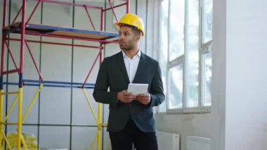 Man architect looking carefully around in the construction site analysing the plan of construction wearing protective helmet. 4K