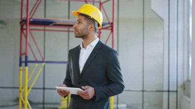 In front of the camera at construction site businessman in a suit MAN looking around analysing the plan of work holding a digital tablet in hands. 4K
