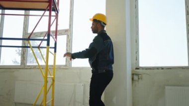 Charismatic constructor worker in the uniform and safety helmet take the mobile ladder from aluminium and roller down through the construction site.