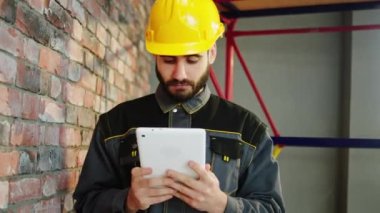 Charismatic foreman with safety equipment and helmet take a look over the end of renovations from his project he looking through the digital tablet to make some modifications. 4k