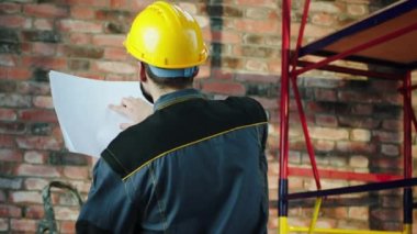 Concentrated working foreman at construction site he using the plan of construction to analysing and check if it s right everything he wearing protective helmet and equipment. 4k